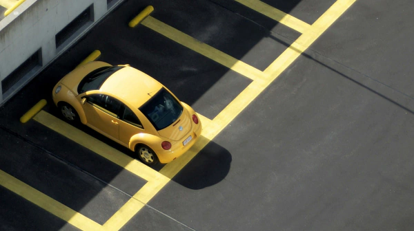 Zdjęcie parkingu z lotu ptaka z wieloma pustymi miejscami i tylko jednym zajętym miejscem, w który stoi zaparkowany żółty samochód.