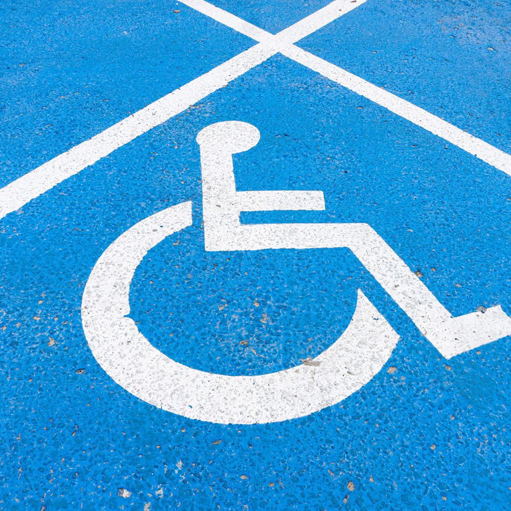 Symbol miejsca parkingowego dla osób z niepełnosprawnością na niebieskiej nawierzchni