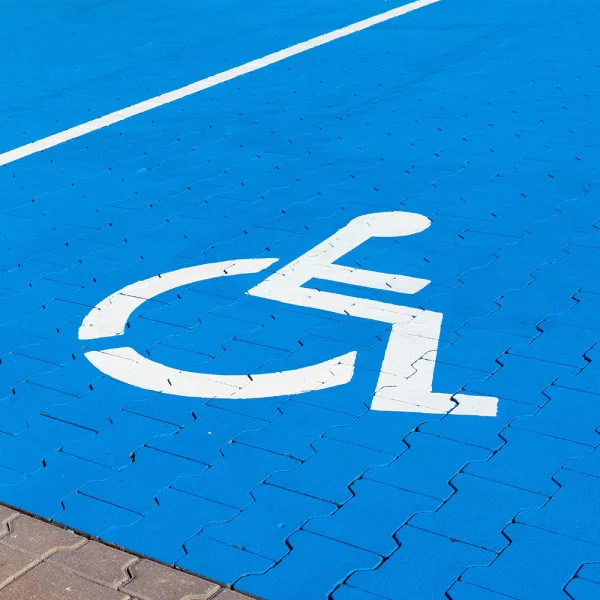 kostka brukowa w niebieskim kolorze, która nawiązuje do miejsca dla osób z niepełnosprawnościami. Na tym biała ikonografia z symbolem osoby niepełnosprawnej na wózku inwalidzkim