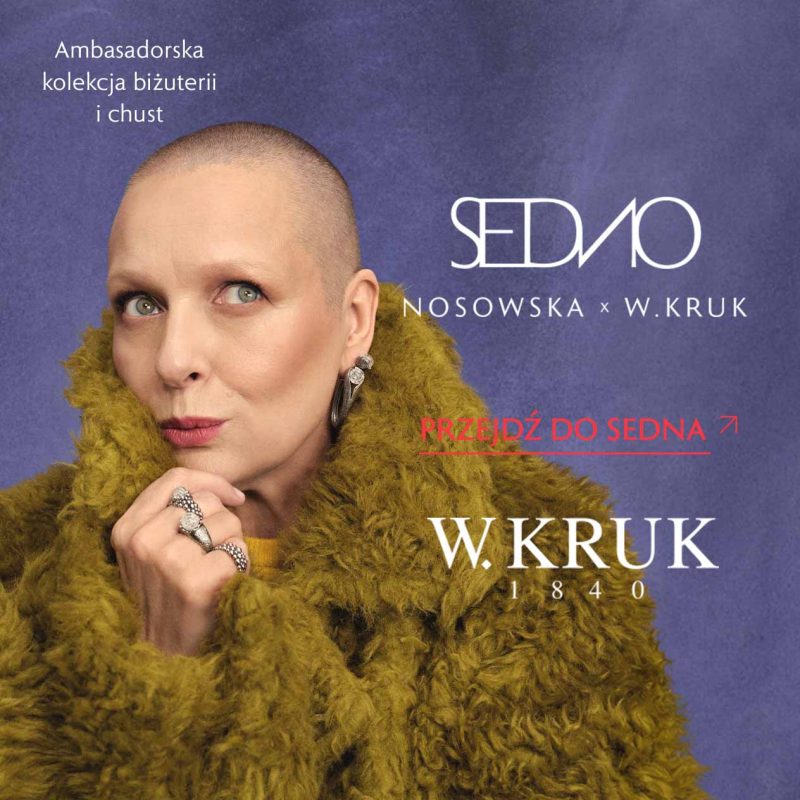 Katarzyna Nosowska w puszystym oliwkowym okryciu prezentuje kolczyki i pierścionki w srebrnym kolorze, opierając dłoń pod brodą. Na fioletowym tle napisy „SEDNO NOSOWSKA x W.KRUK”, „Ambasadorska kolekcja biżuterii i chust”, „Przejdź do SEDNA” oraz logo W.KRUK.